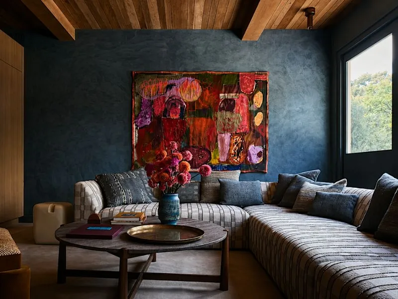 Thiết kế phòng khách phong cách hiện đại đặt sofa góc dưới bức tranh nhiều màu trên nền tường tối.