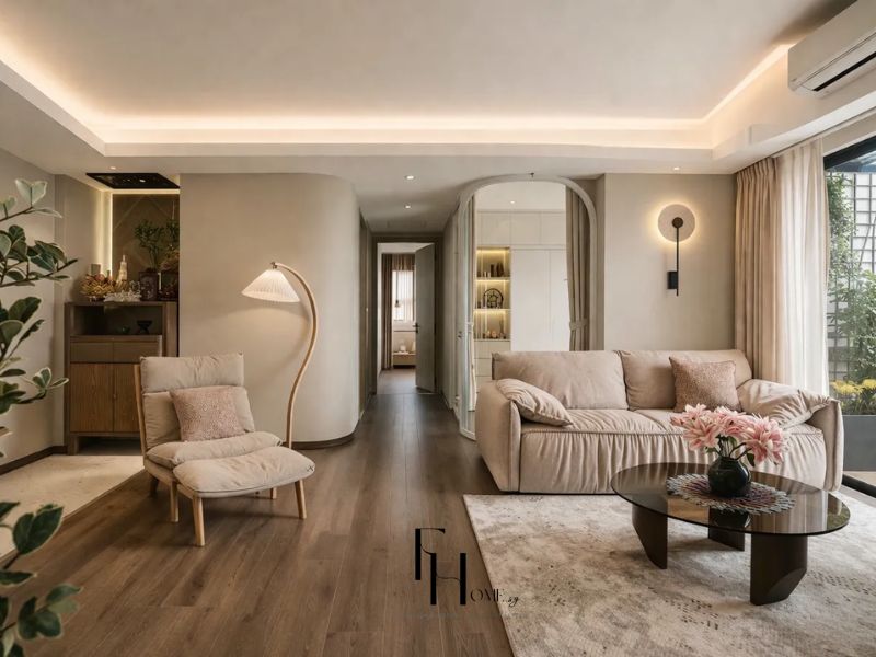 Phòng khách phong cách Wabi Sabi tông be ấm, sofa bồng bọc vải, bàn trà kính chân gỗ tự nhiên và vòm cung tròn dẫn vào hành lang trong thiết kế nội thất căn hộ 90m2