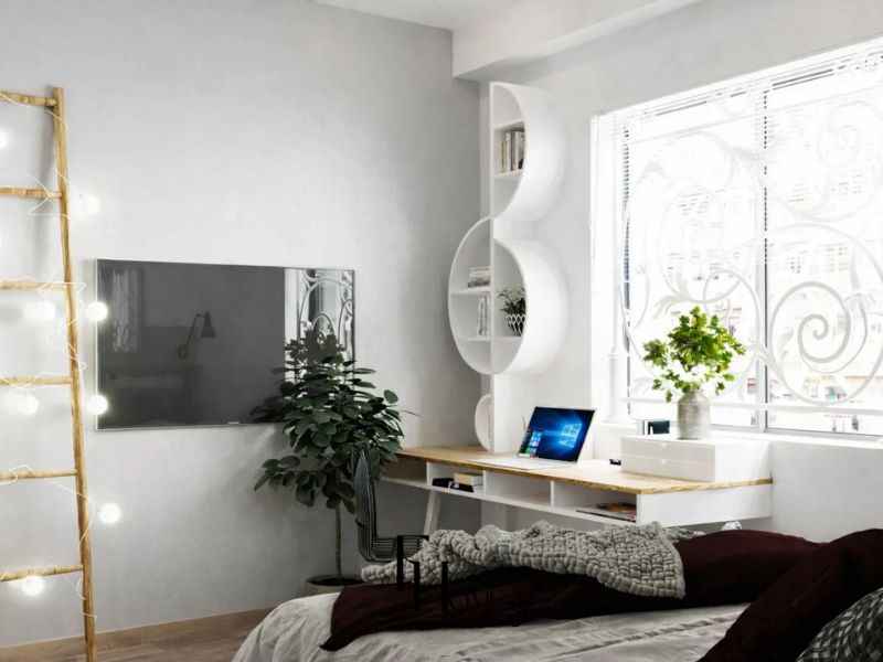 Góc làm việc bàn gỗ gắn tường, kệ tròn trắng và cây xanh cửa sổ giữ không gian thoáng sáng