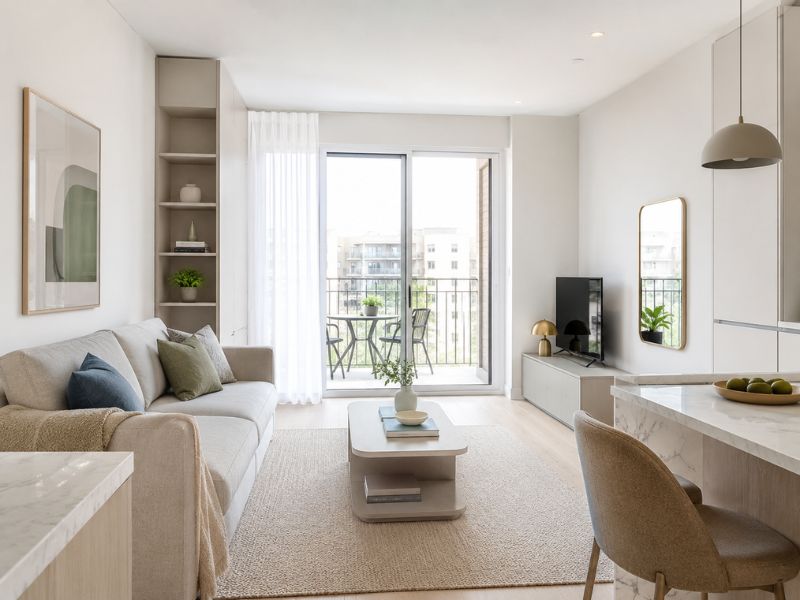 Thiết kế nội thất căn hộ 45m2 với màu trắng sáng chiếm ưu thế, sofa be, gối xanh – xám điểm nhấn và phòng khách liên thông ban công