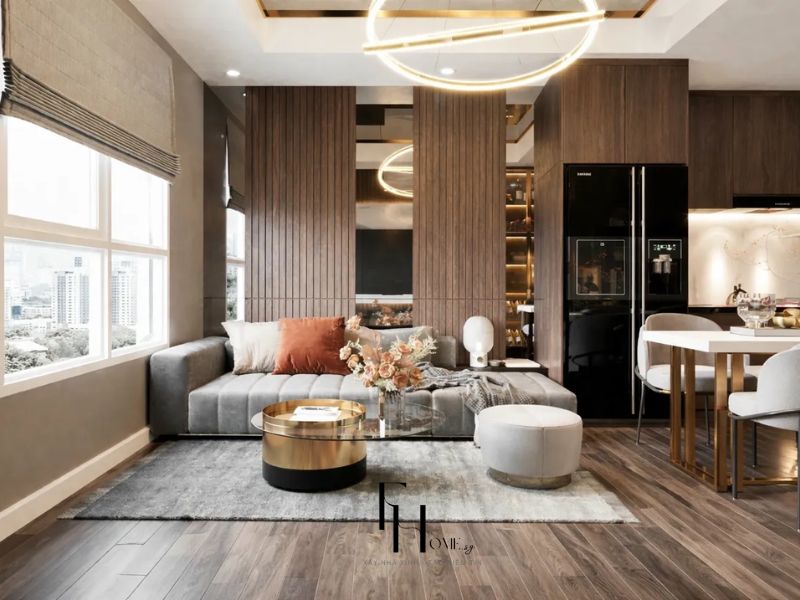 Phòng khách liền bếp chung cư 68m2 phân vùng bằng thảm xám và vách ốp gỗ nan dọc thay vách ngăn cứng, đèn chùm vòng tròn vàng đồng xác định khu ngồi