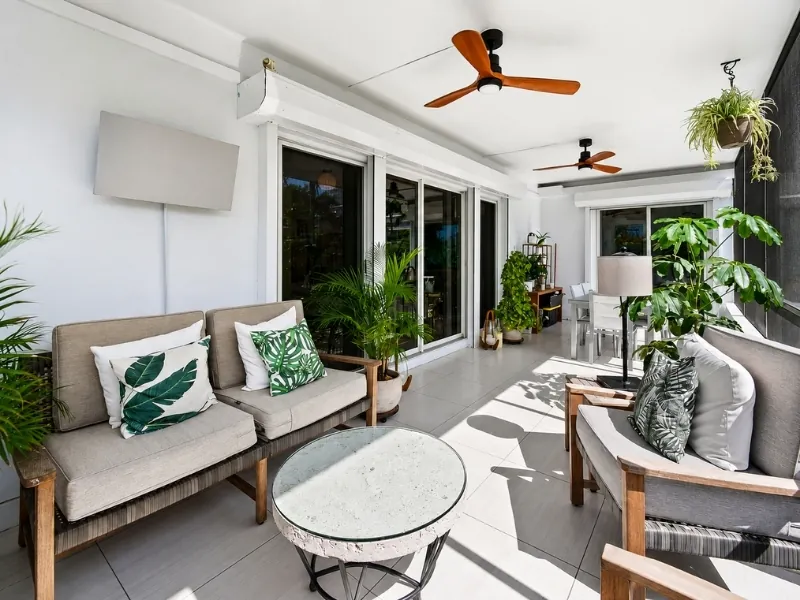 Lô gia phong cách Tropical với sofa tông trung tính, gối họa tiết lá và cây xanh.