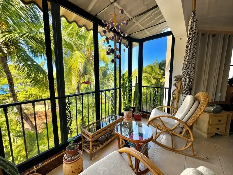 Lô gia phong cách Tropical với ghế mây tre và tầm nhìn hàng dừa.