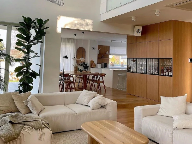 Phòng khách chung cư tối giản với sofa trắng tủ gỗ liền tường và cây xanh lớn