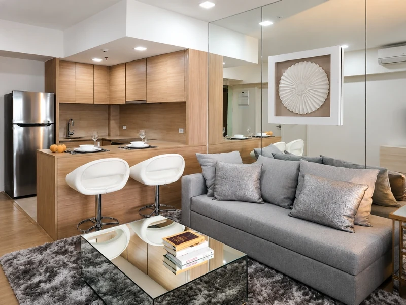 Phòng khách chung cư 45m2 với sofa xám, bàn trà gương, bếp mở và gương lớn sau sofa.