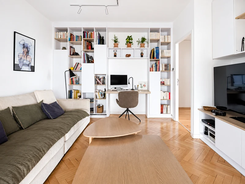 Phòng khách chung cư có góc làm việc với bàn gỗ, kệ sách trắng và sofa xanh.