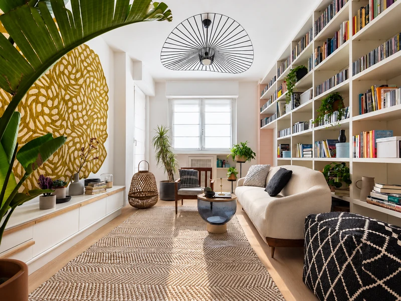 Phòng khách chung cư với kệ sách lớn, sofa trắng, thảm woven và trần quạt độc đáo.