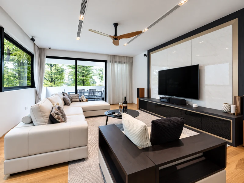 Phòng khách hiện đại với sofa chữ L, bàn trà đen và kệ tivi treo tường.