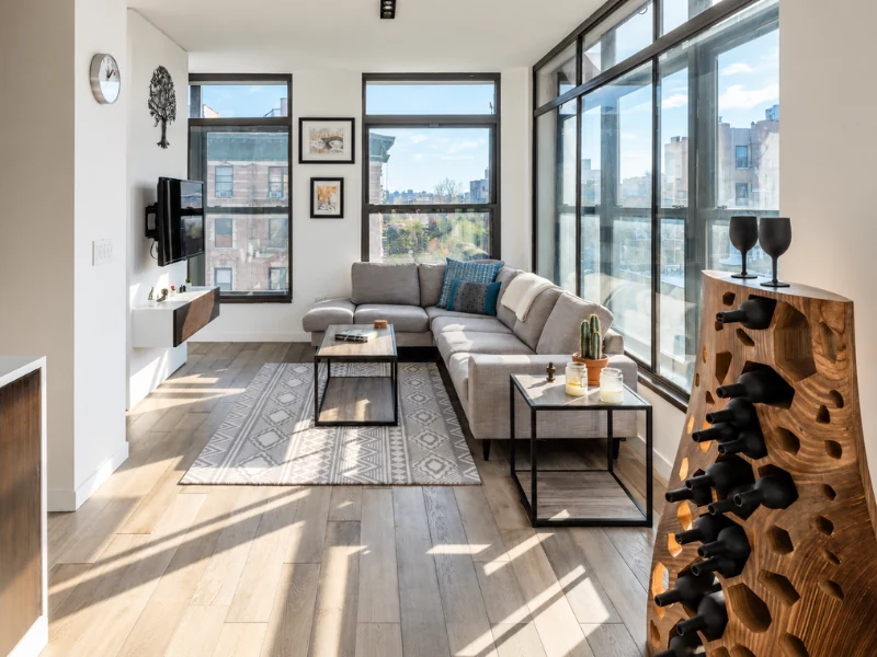 Phòng khách hiện đại với sofa chữ L, kệ tivi treo tường và không gian ngập ánh sáng tự nhiên.