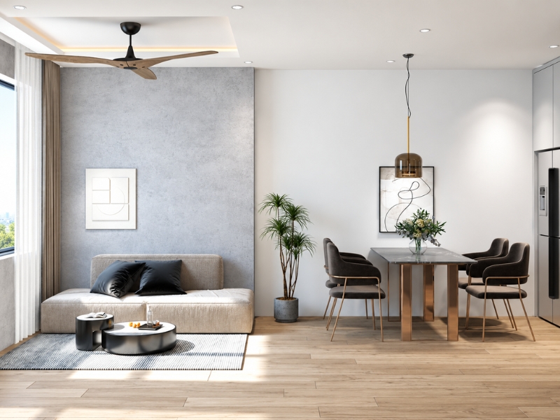 Không gian phòng khách và bàn ăn căn hộ tối giản với sofa sáng màu, bàn gỗ, cây xanh và quạt trần.
