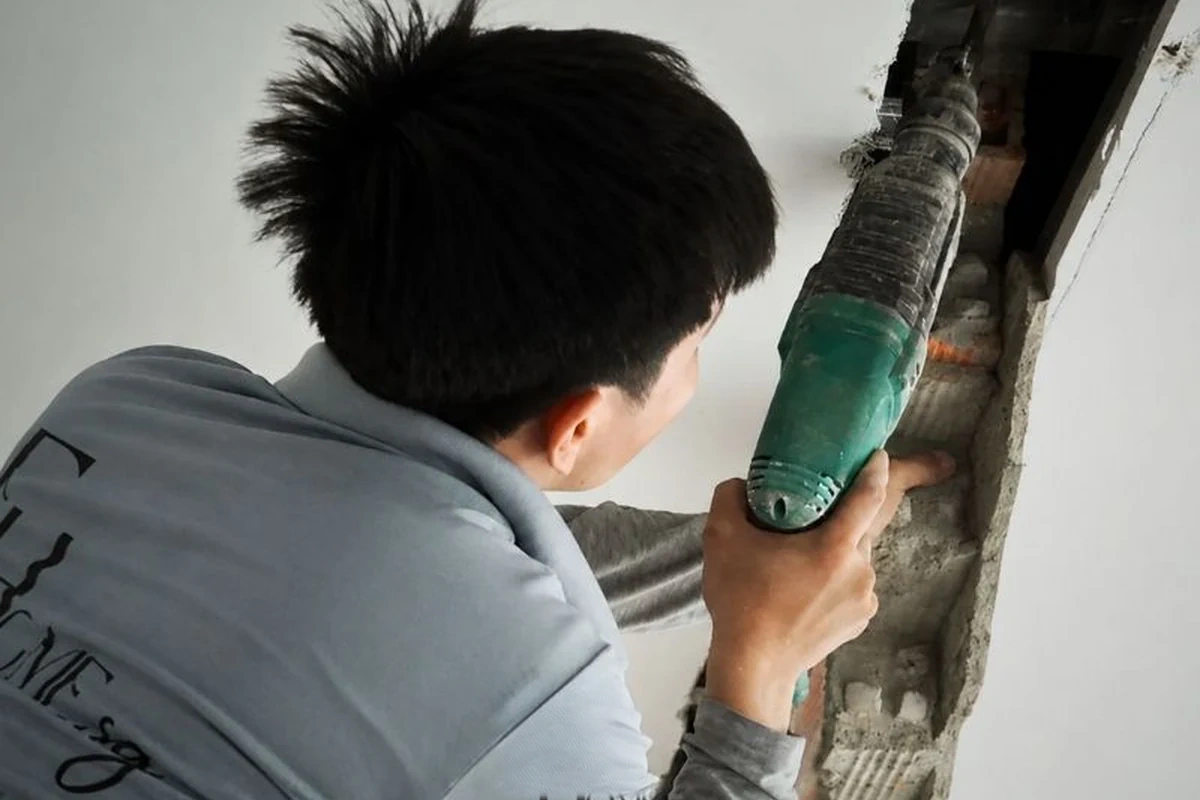 Thợ thi công dùng máy đục tạo rãnh kỹ thuật trên tường căn hộ